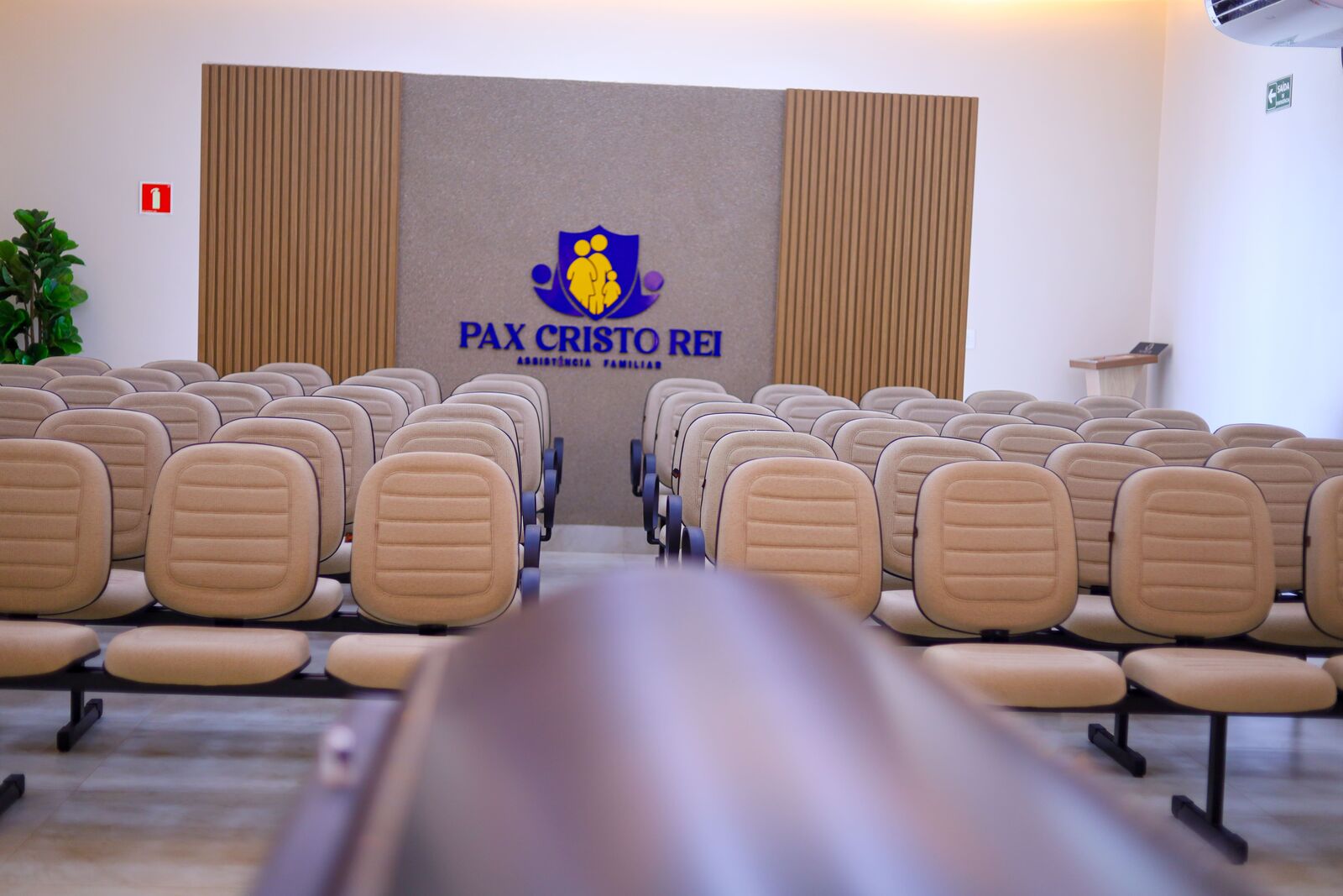 Assentos da capela voltados para o painel com o brasão Pax Cristo Rei